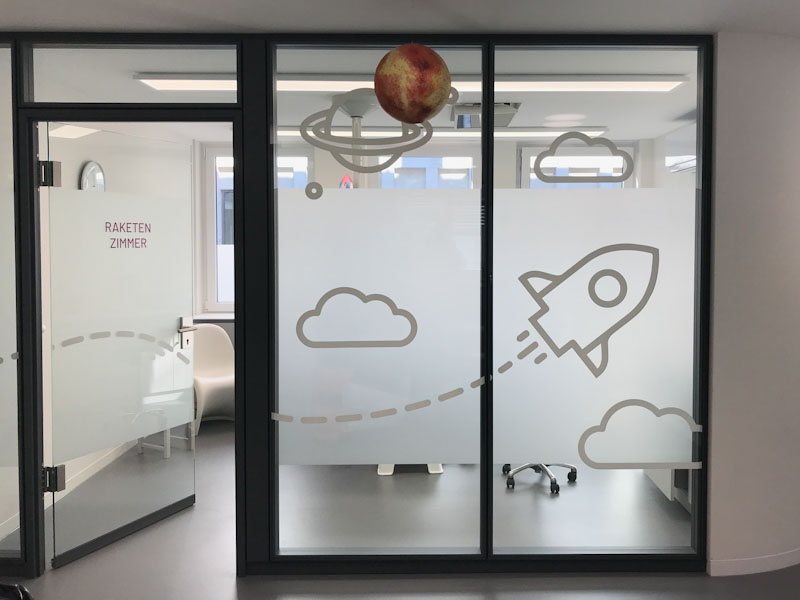Folienbeschriftung einer Glaswand mit weißer Folie und Glasdekorfolie, Wolken, Planeten und Rakete Kinderzahnheilkunde